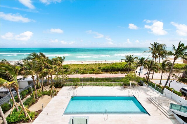 view of swimming pool featuring a water view, a patio, and a view of the beach