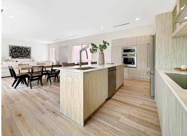 kitchen with sink, stainless steel appliances, an island with sink, light wood-type flooring, and light brown cabinets