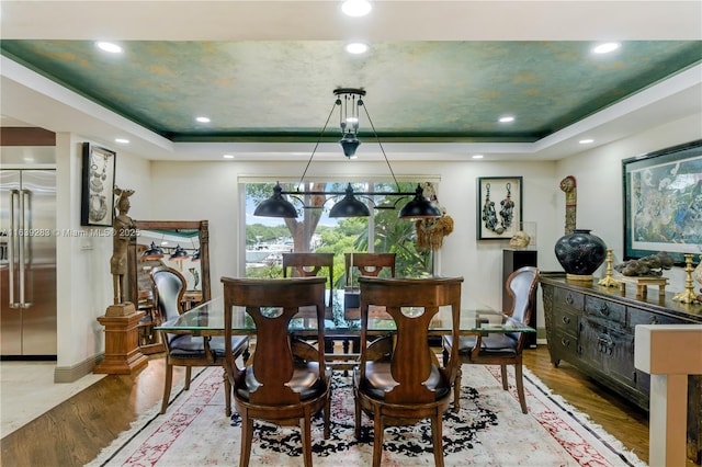 dining room with baseboards, wood finished floors, a raised ceiling, and recessed lighting