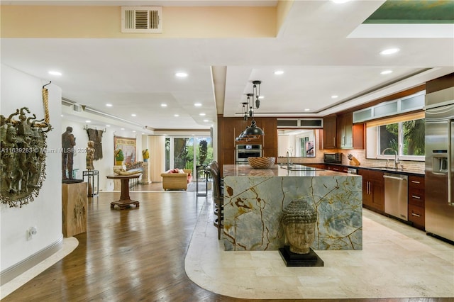 kitchen with stainless steel appliances, a sink, visible vents, light wood-type flooring, and decorative backsplash