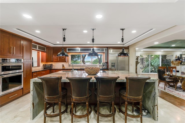 kitchen featuring light stone countertops, tasteful backsplash, appliances with stainless steel finishes, and a spacious island