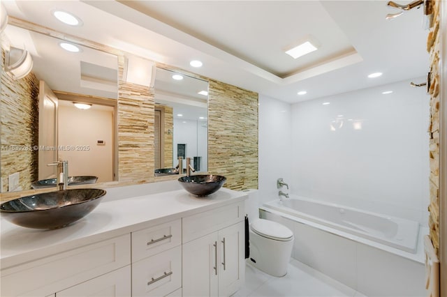 full bathroom with toilet, a tray ceiling, a sink, and a bath