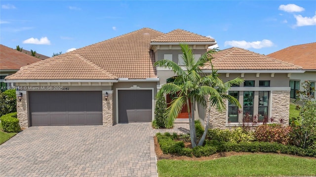 mediterranean / spanish house featuring decorative driveway, stone siding, an attached garage, and stucco siding