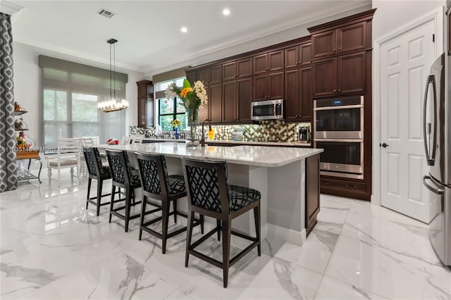 kitchen featuring backsplash, a center island with sink, crown molding, hanging light fixtures, and stainless steel appliances