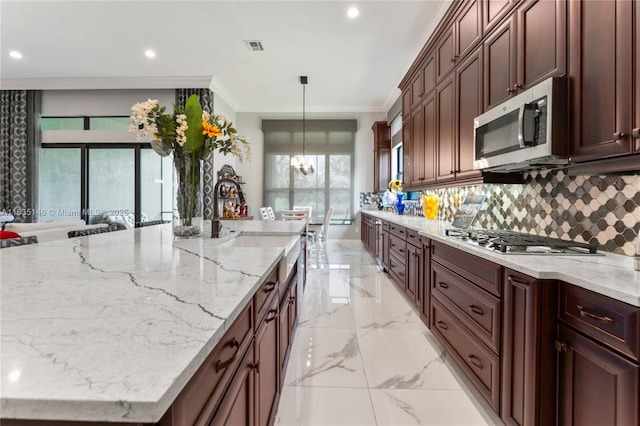 kitchen with pendant lighting, ornamental molding, appliances with stainless steel finishes, a notable chandelier, and light stone counters