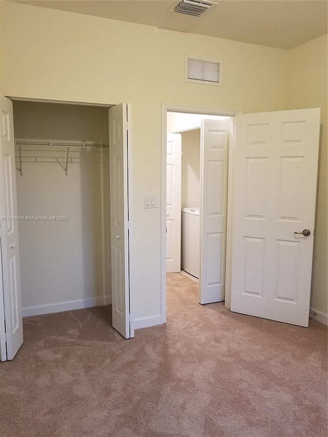 unfurnished bedroom with a closet, washer / clothes dryer, and light colored carpet