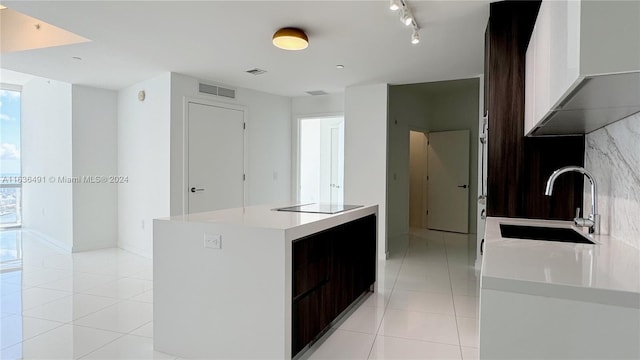 kitchen featuring a center island, sink, black electric cooktop, light tile patterned floors, and dark brown cabinets