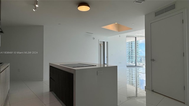 kitchen with a center island, light tile patterned flooring, black electric cooktop, and a wall of windows