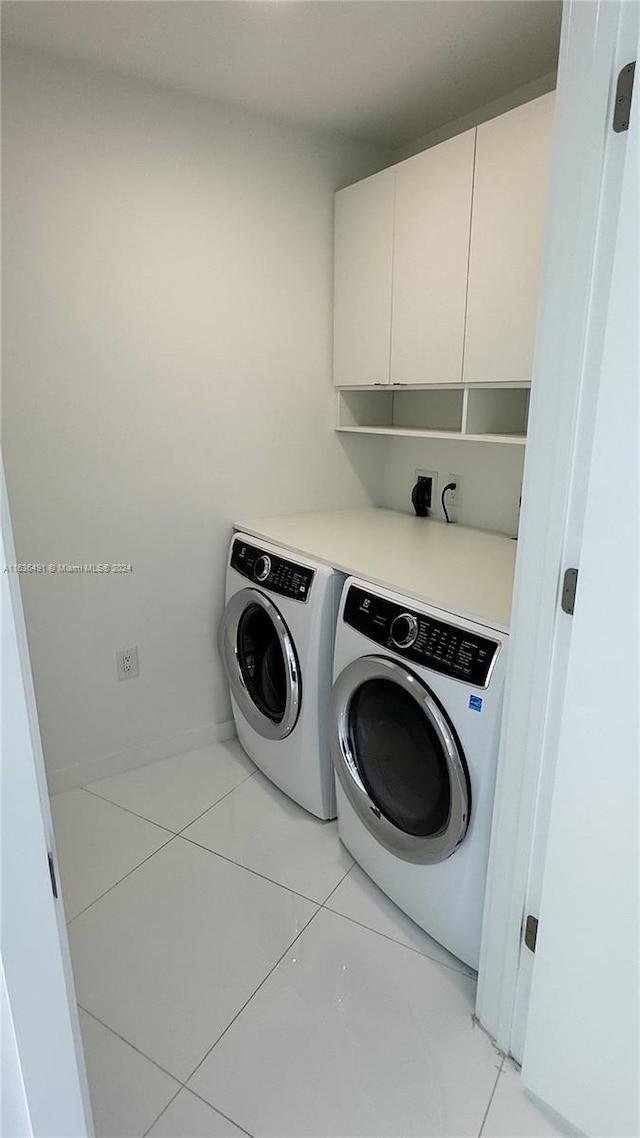 clothes washing area featuring cabinets, light tile patterned floors, and washing machine and clothes dryer