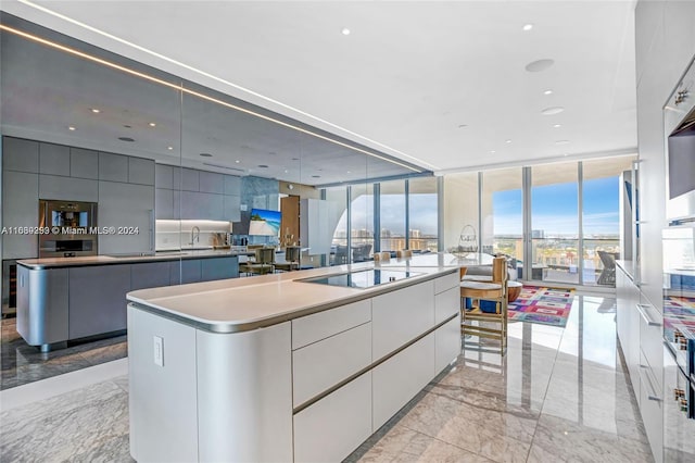 kitchen featuring expansive windows, black electric stovetop, light tile patterned floors, an island with sink, and sink