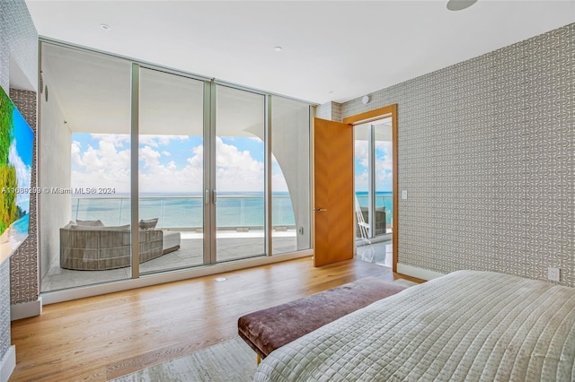 bedroom featuring access to outside, a water view, floor to ceiling windows, and light hardwood / wood-style floors