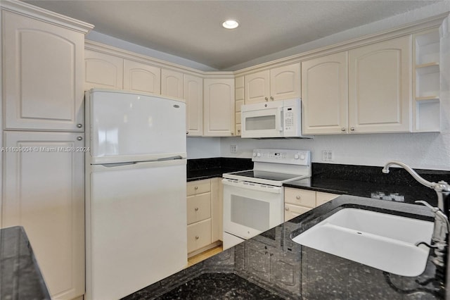 kitchen with cream cabinetry, sink, white appliances, and dark stone counters