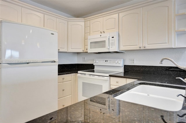 kitchen with cream cabinets, sink, dark stone countertops, and white appliances