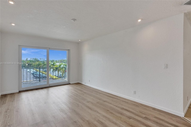 empty room with a textured ceiling and light hardwood / wood-style flooring