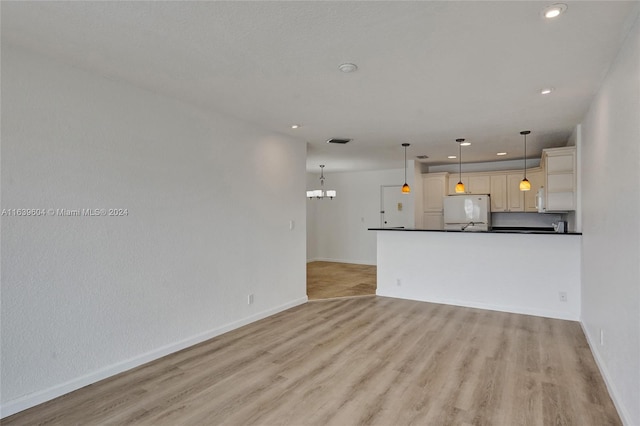 unfurnished living room featuring an inviting chandelier and light hardwood / wood-style flooring