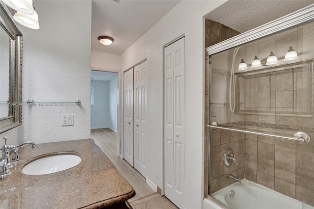 bathroom featuring vanity, shower / bath combination with glass door, and a textured ceiling