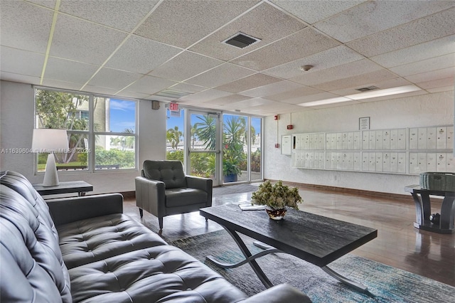 living room with wood-type flooring, a drop ceiling, and a mail area