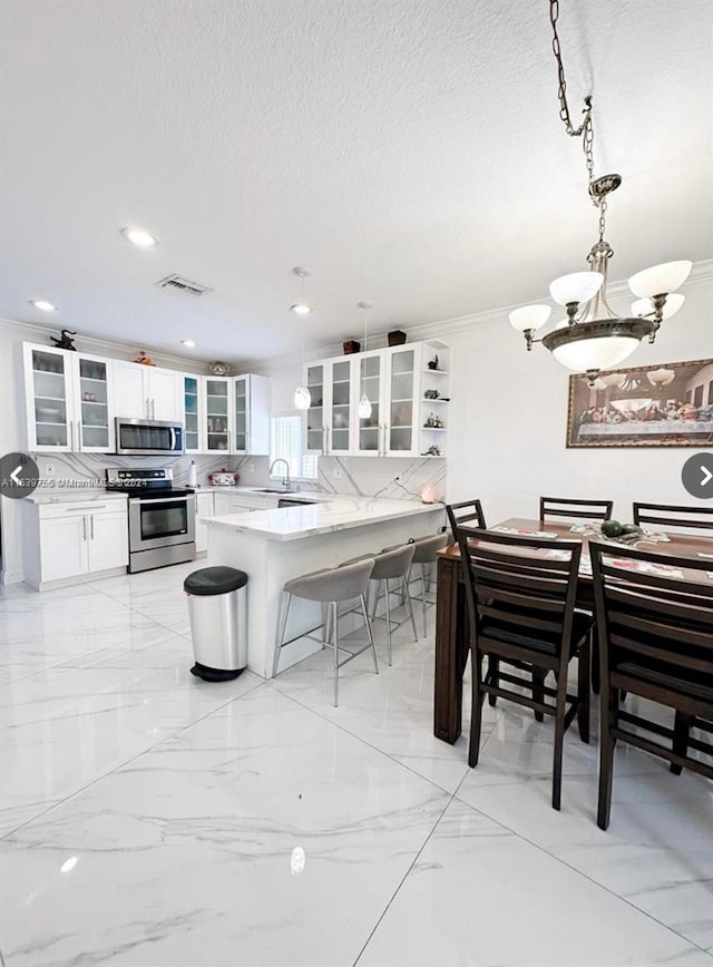 kitchen with appliances with stainless steel finishes, a breakfast bar, pendant lighting, white cabinets, and kitchen peninsula