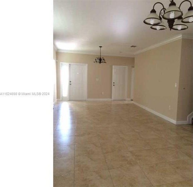 tiled empty room with a notable chandelier and crown molding