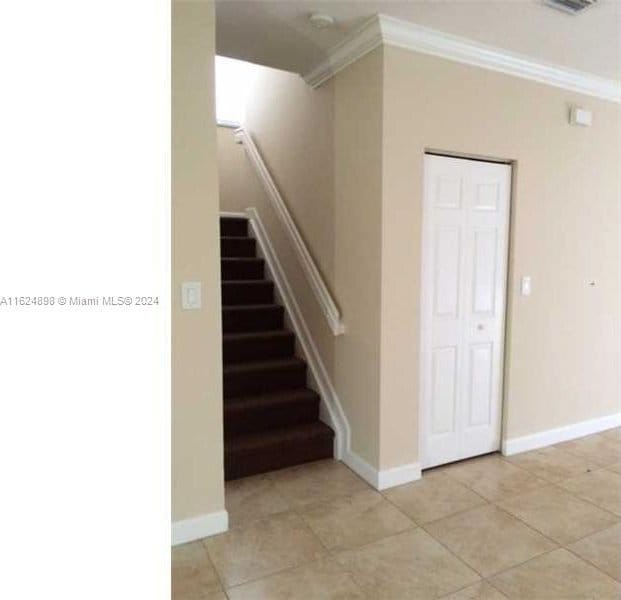 staircase with crown molding and tile patterned floors