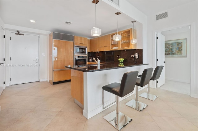 kitchen with kitchen peninsula, built in appliances, a breakfast bar, and hanging light fixtures