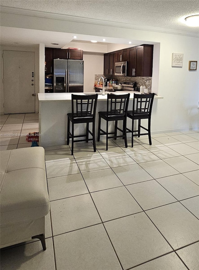 kitchen with tasteful backsplash, a breakfast bar, appliances with stainless steel finishes, a textured ceiling, and light tile patterned flooring