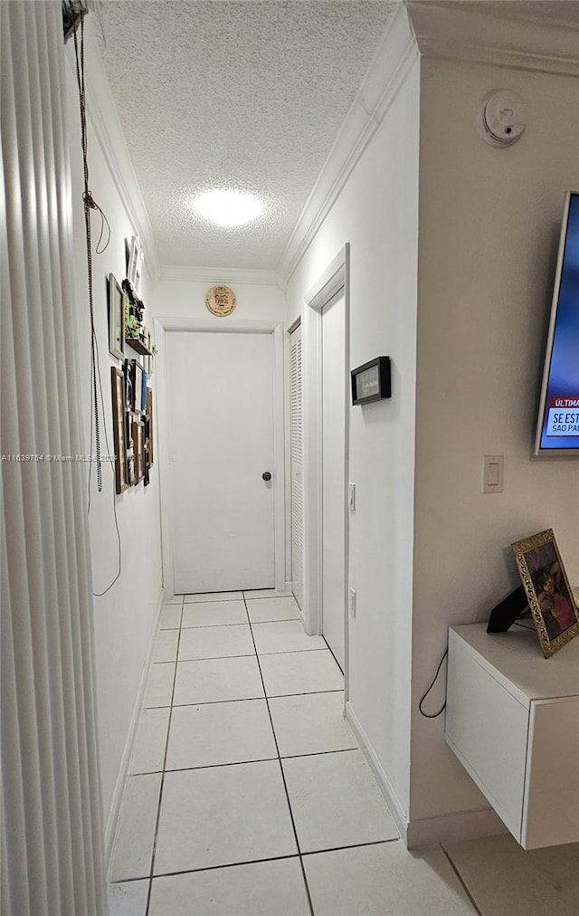 hallway featuring a textured ceiling, light tile patterned flooring, and ornamental molding