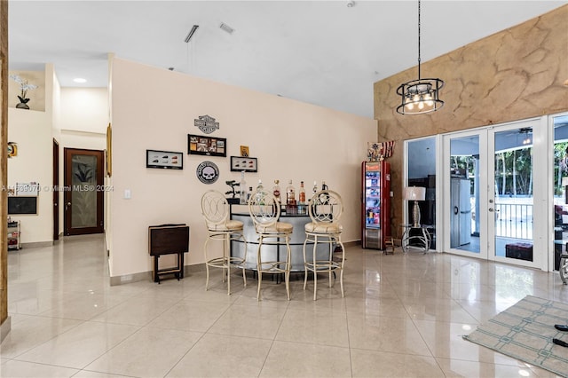 interior space with a towering ceiling, light tile patterned flooring, french doors, and a chandelier