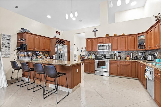 kitchen with stainless steel appliances, light tile patterned floors, light stone countertops, backsplash, and decorative light fixtures