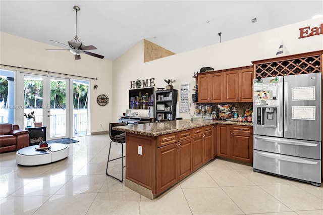 kitchen with dark stone countertops, stainless steel refrigerator with ice dispenser, a kitchen breakfast bar, ceiling fan, and kitchen peninsula