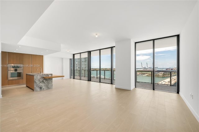 unfurnished living room featuring sink, floor to ceiling windows, a water view, and light wood-type flooring