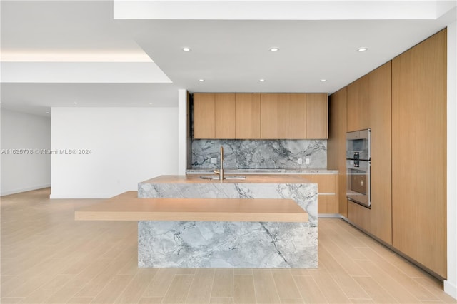 kitchen featuring modern cabinets, a sink, a kitchen island with sink, light countertops, and backsplash