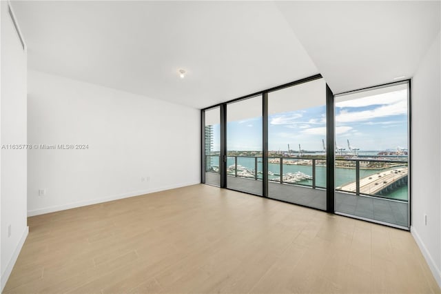 spare room featuring a water view, light wood-type flooring, baseboards, and a wall of windows