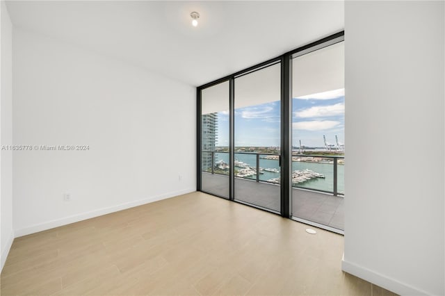 empty room featuring floor to ceiling windows, a water view, and light wood-type flooring