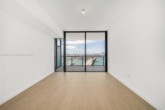 spare room with light wood-type flooring, expansive windows, a water view, and baseboards