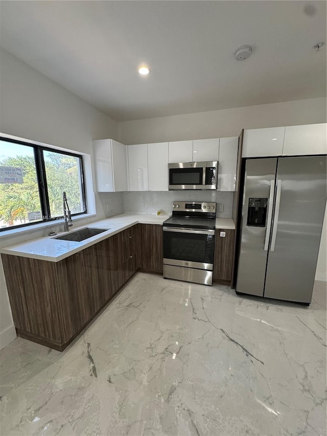 kitchen featuring white cabinets, appliances with stainless steel finishes, sink, backsplash, and dark brown cabinets