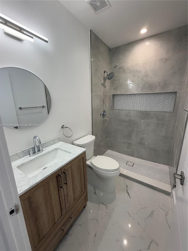 bathroom with a tile shower, toilet, and vanity