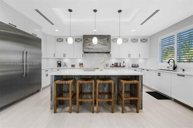 kitchen with white cabinets, built in refrigerator, sink, a raised ceiling, and wall chimney exhaust hood