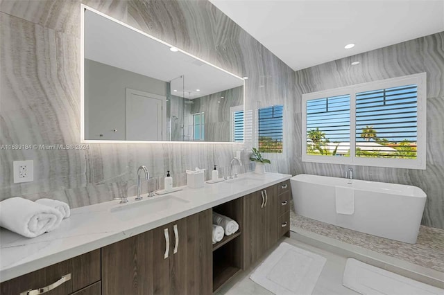 bathroom with tile walls, double vanity, a bathing tub, and tile patterned flooring