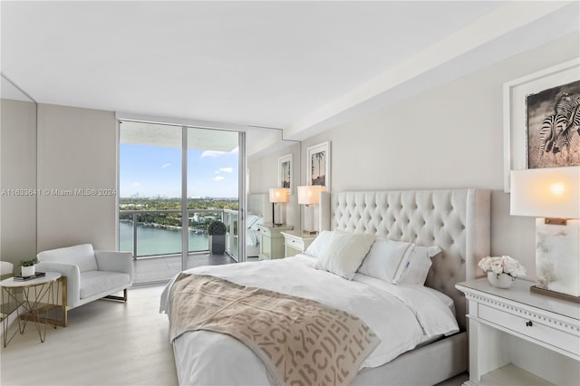 bedroom featuring access to outside, a water view, light wood-type flooring, and a wall of windows