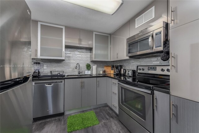 kitchen featuring dark countertops, appliances with stainless steel finishes, gray cabinets, and glass insert cabinets