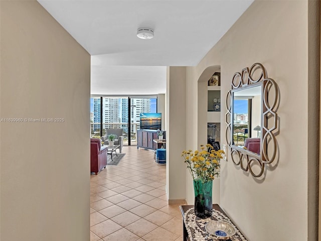 hallway featuring floor to ceiling windows, light tile patterned floors, and arched walkways