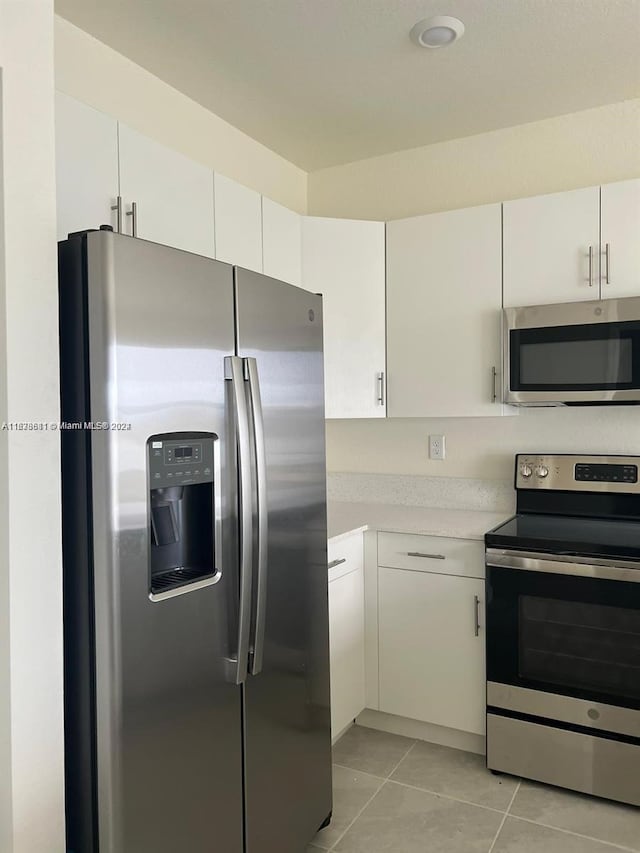 kitchen featuring appliances with stainless steel finishes, light tile patterned flooring, and white cabinets