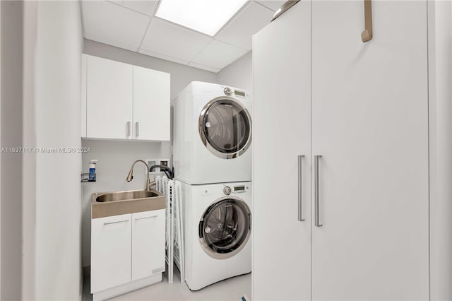 laundry area with sink, stacked washer and clothes dryer, and cabinets