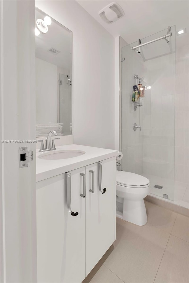 bathroom featuring toilet, a tile shower, vanity, and tile patterned flooring