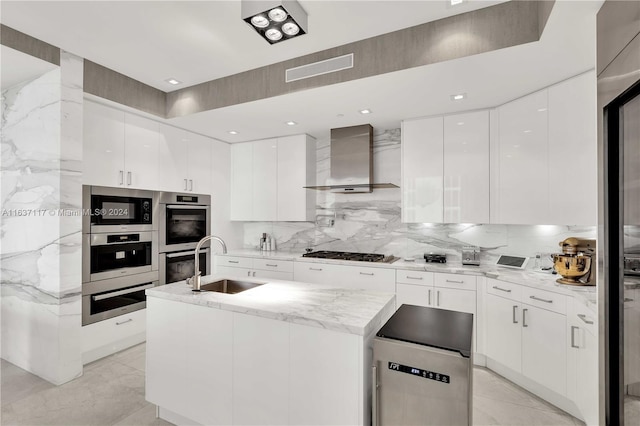 kitchen featuring decorative backsplash, sink, double oven, white cabinetry, and wall chimney exhaust hood