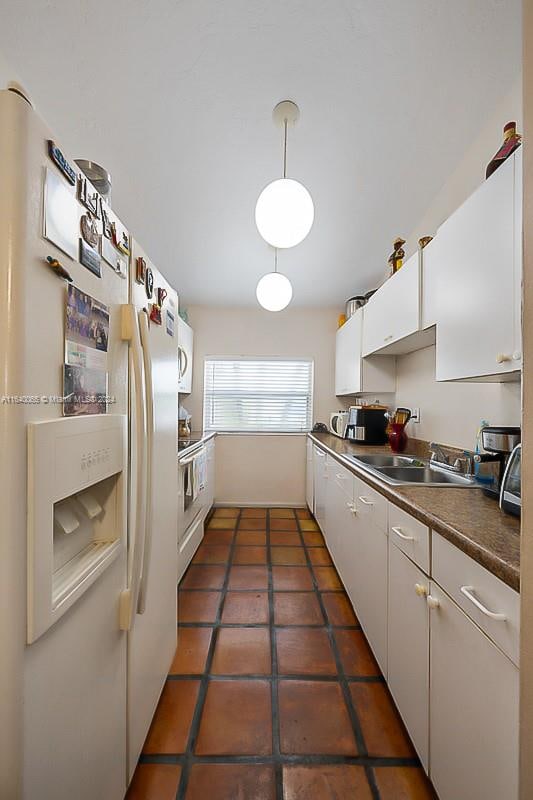 kitchen with dark tile patterned flooring, white appliances, hanging light fixtures, white cabinetry, and sink