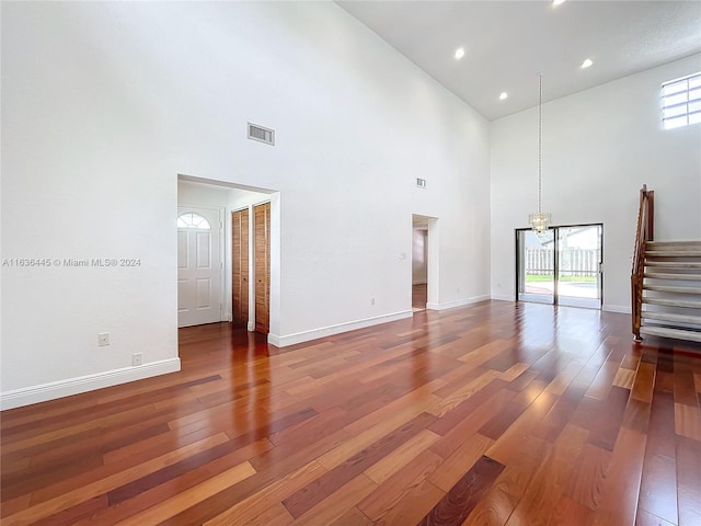 unfurnished living room featuring a notable chandelier, hardwood / wood-style floors, and a high ceiling