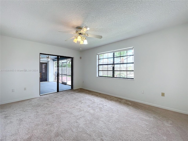 empty room featuring ceiling fan, a wealth of natural light, a textured ceiling, and light carpet