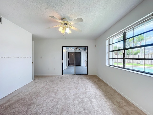 spare room with a textured ceiling, light colored carpet, and ceiling fan